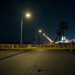 Cinematic wide-angle shot of the Santa Monica Pier at night, with police lights reflecting the somber mood after a shooting incident during a large fight.
